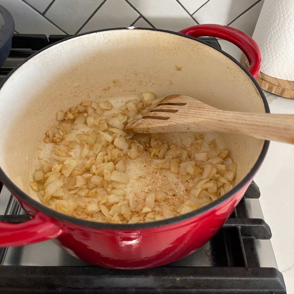 Sautéing onion and garlic with flour in a dutch oven with a wooden spatula on a gas stove.