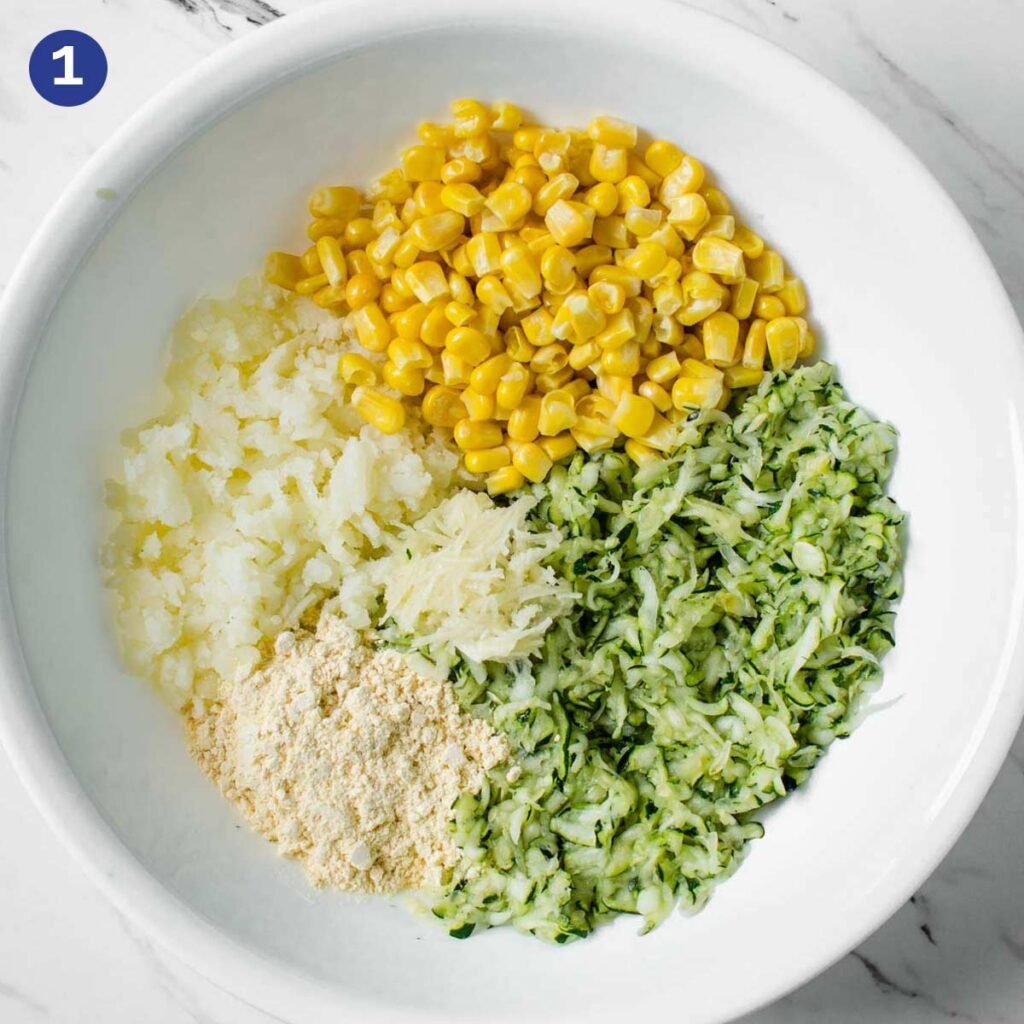 Shredded zucchini, corn, mashed potato, and other ingredients in a mixing bowl.