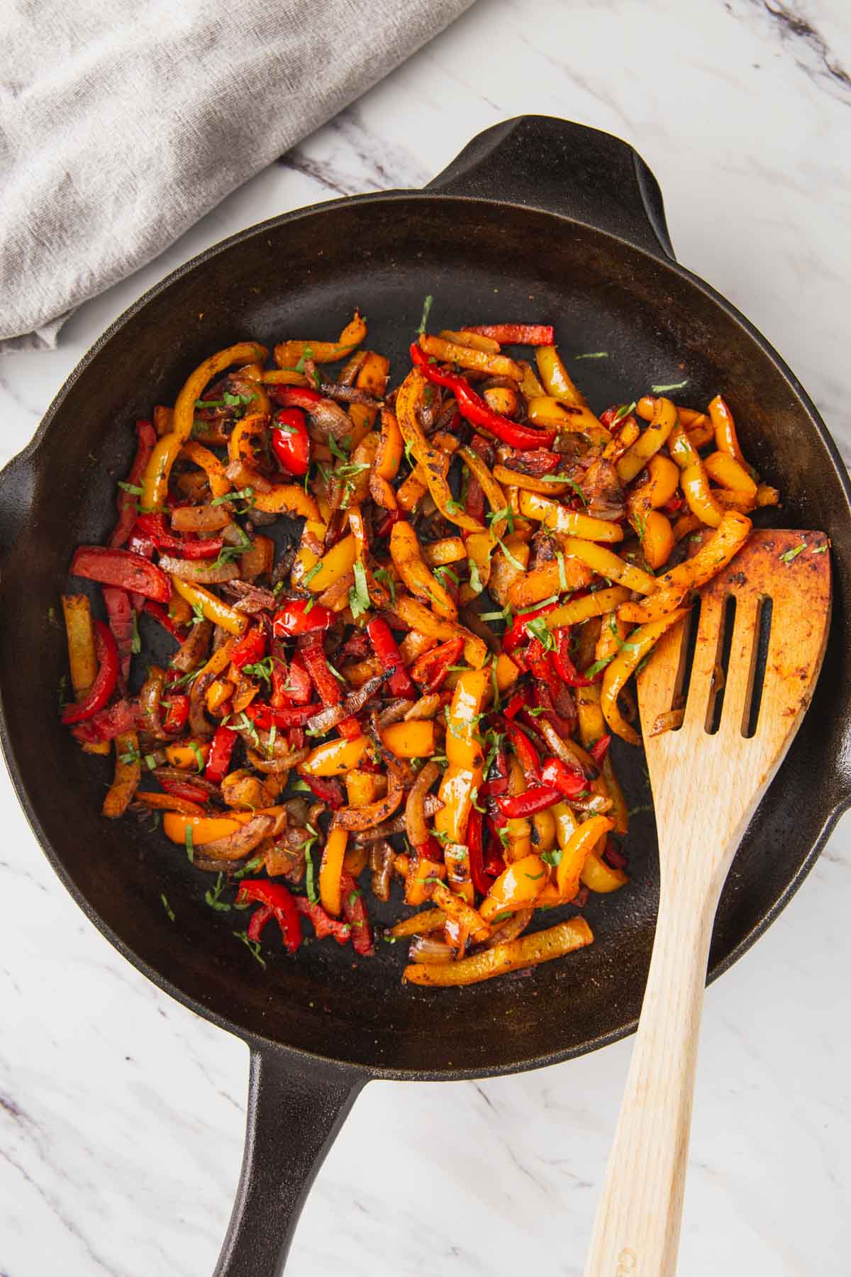 Roasted fajita vegetables in a cast iron pan with a wooden spatula.