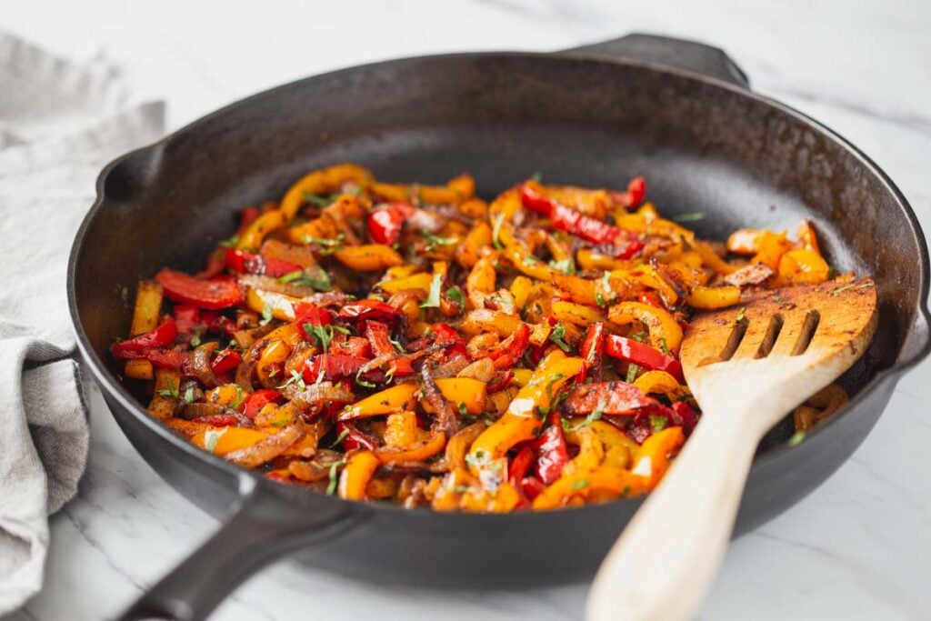 Roasted fajita vegetables in a cast iron pan with a wooden spatula.