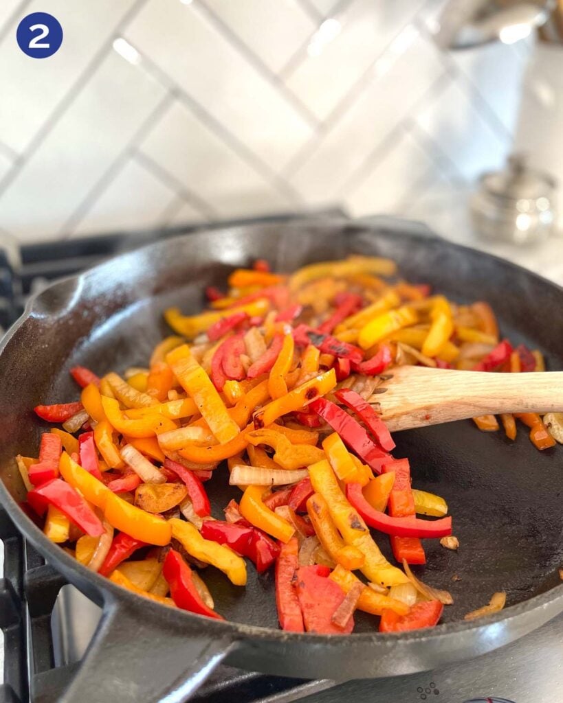 Roasting sliced onion and peppers in a cast iron pan on a gas stove.