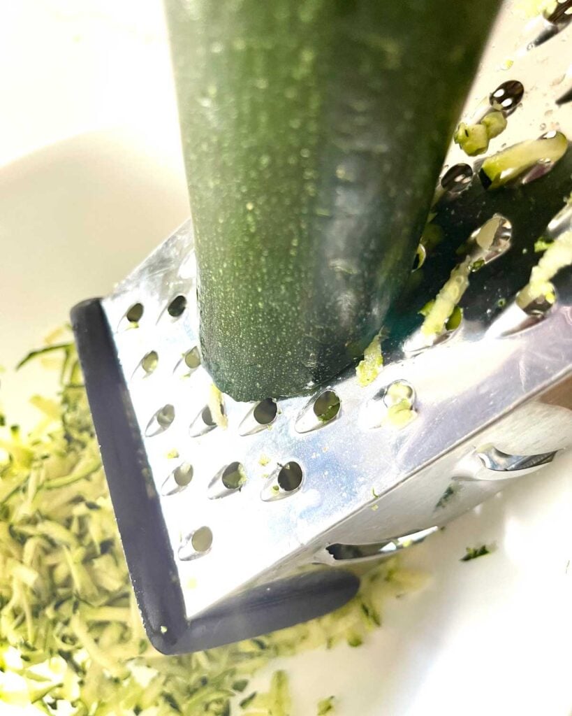 Process shot of shredding zucchini on a box grater.