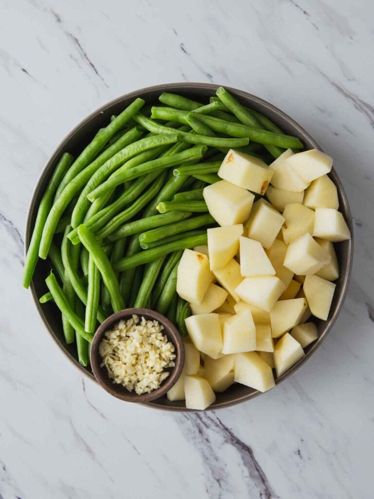 Diced potatoes, trimmed green beans and chopped garlic in a large dish. 