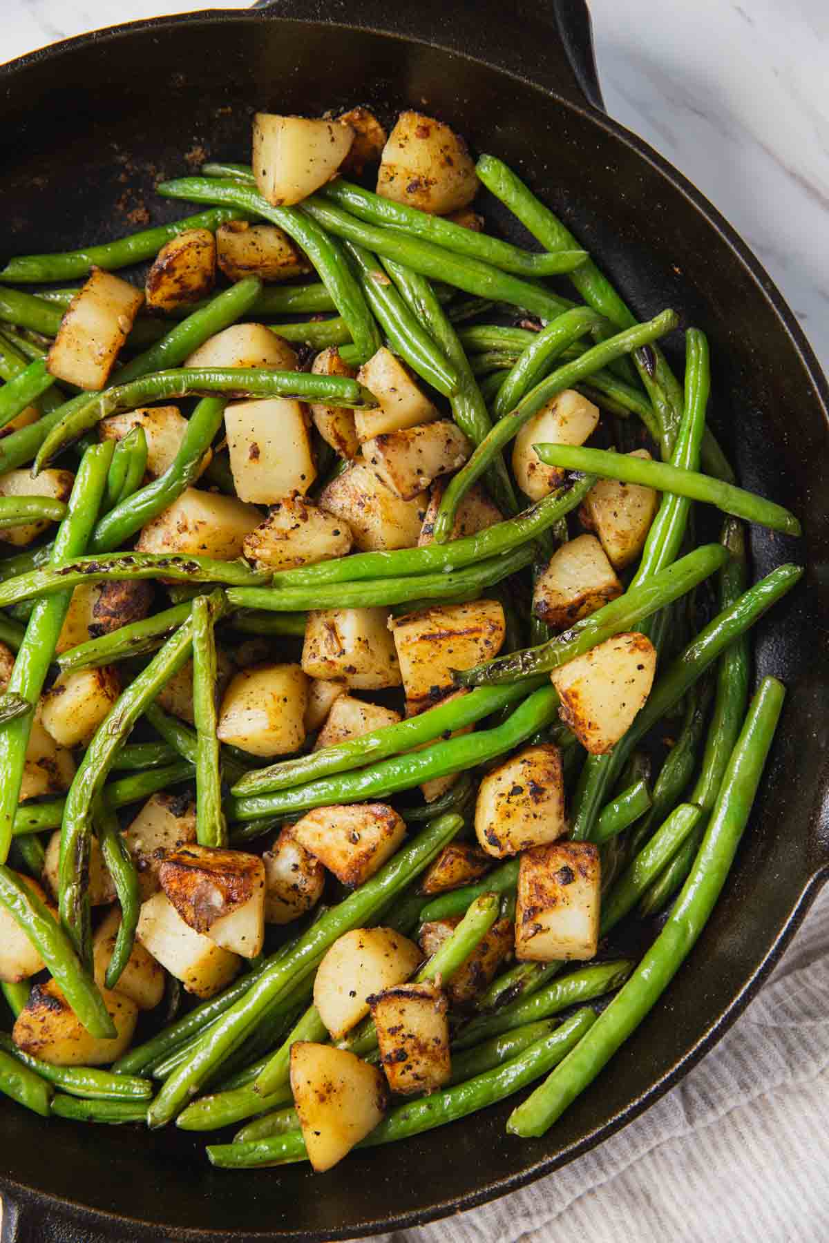 Roasted green beans and potatoes in a cast iron pan after cooking. 