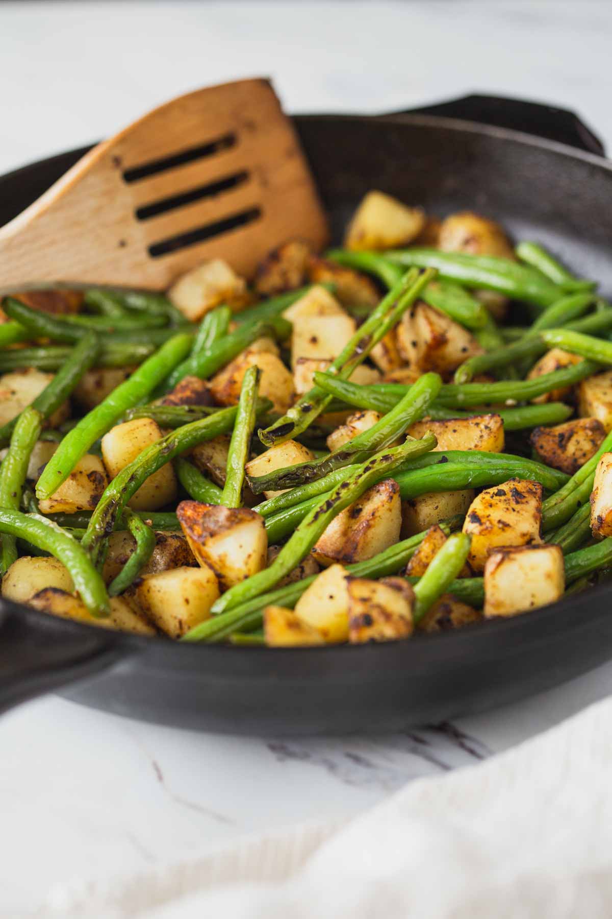 Roasted green beans and potatoes in a cast iron pan after cooking. 
