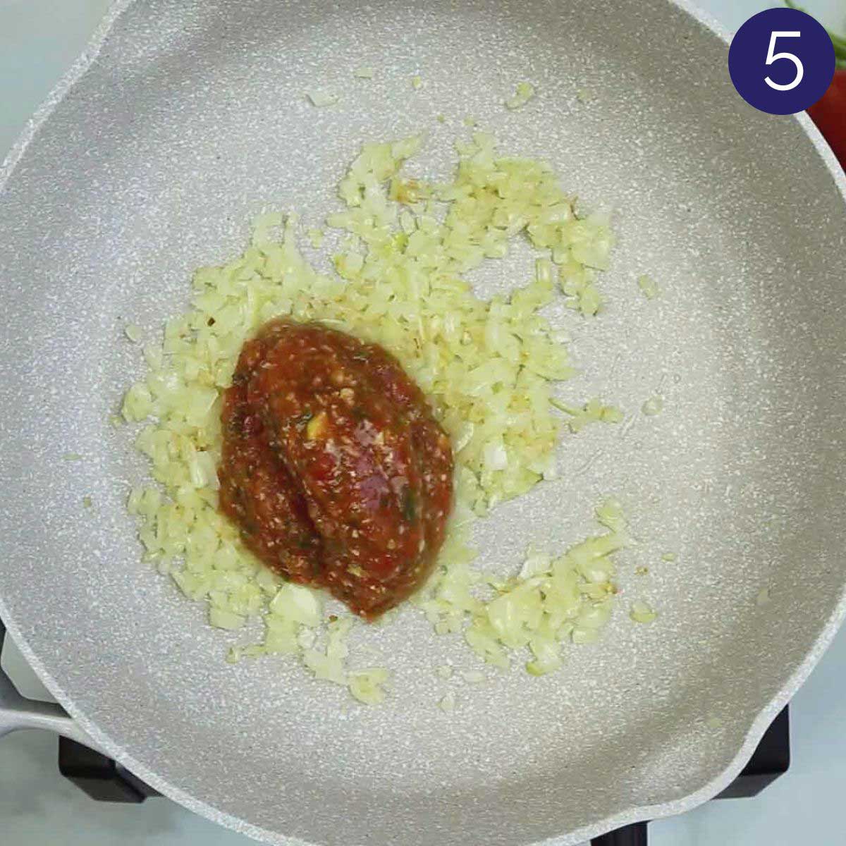 Sautéing diced onion and tomato puree in oil in a large skillet for making shrimp curry.