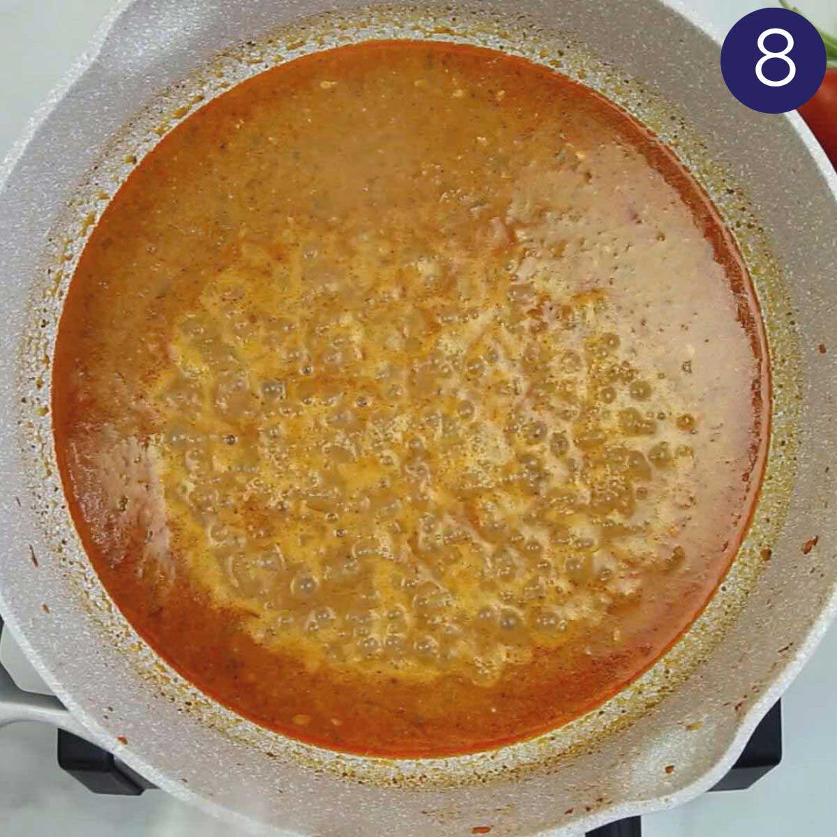 Cooked shrimp curry base with coconut milk, onion, and tomato in a skillet.