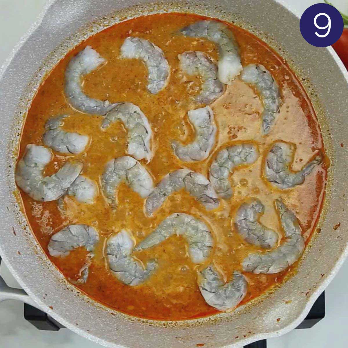 Raw shrimp added to the cooked curry base in a skillet.