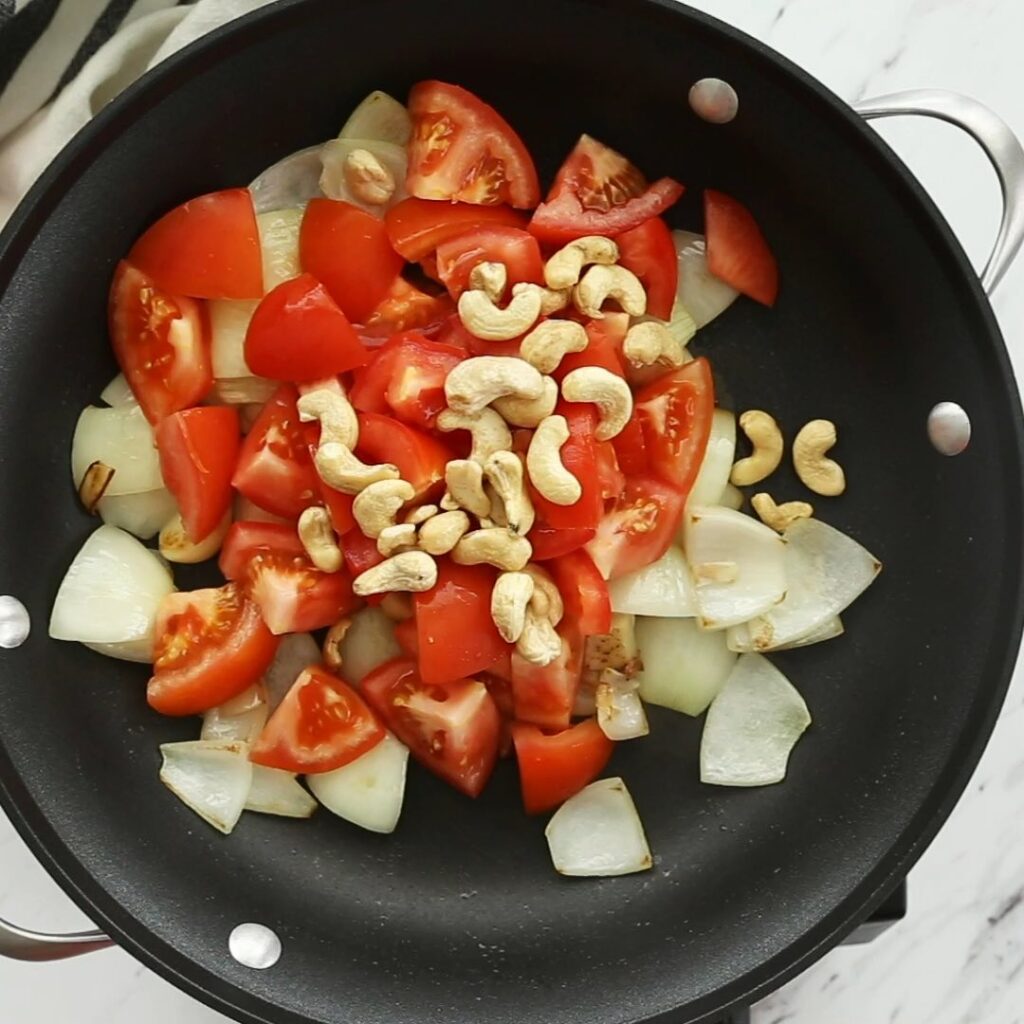 Diced onion, tomato and raw cashews in a large skillet before cooking.