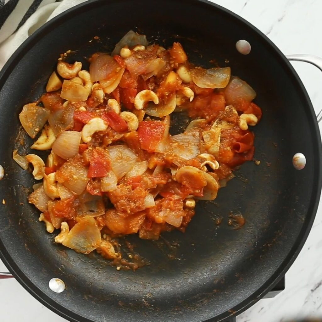 Diced onion, tomato and raw cashews in a large skillet after sautéing.
