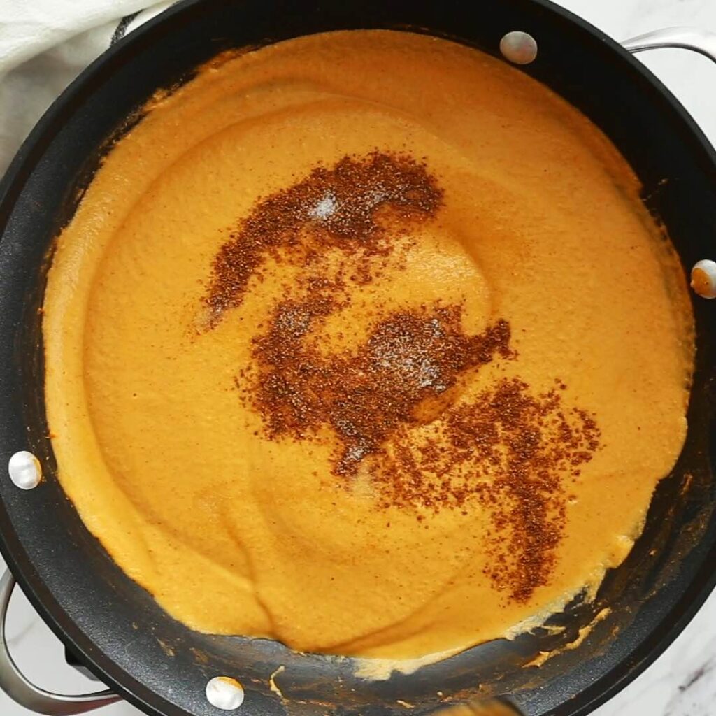 Cooking pureed onion and tomato mixture with garam masala in a skillet.