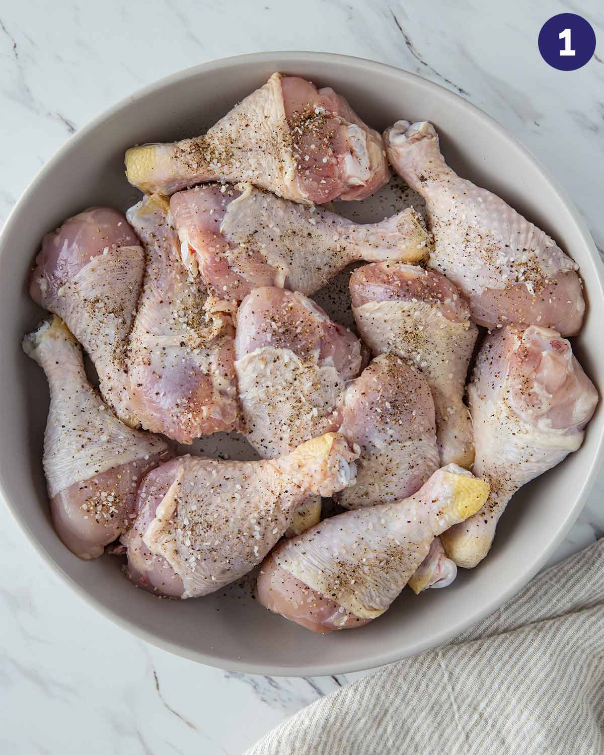 Chicken drumsticks rubbed with salt and pepper in a mixing bowl.