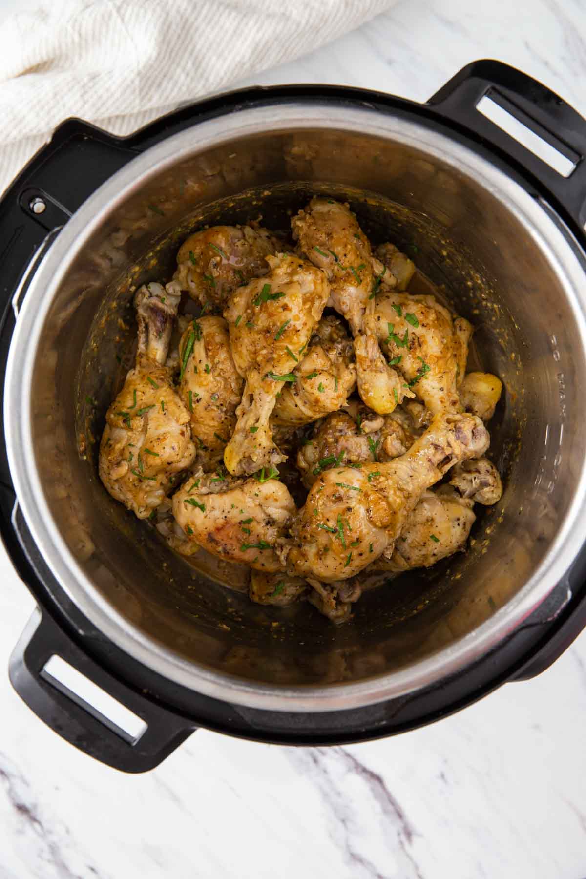 Chicken drumsticks in Instant Pot coated with lemon garlic sauce and garnished with fresh parsley.