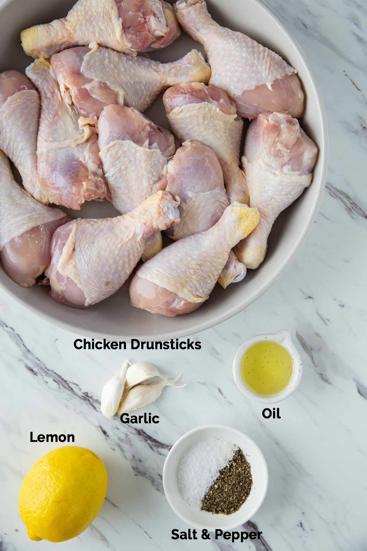 Raw chicken drumsticks, garlic, lemon, oil, salt pepper laid on a flat surface for making Instant Pot chicken drumsticks.