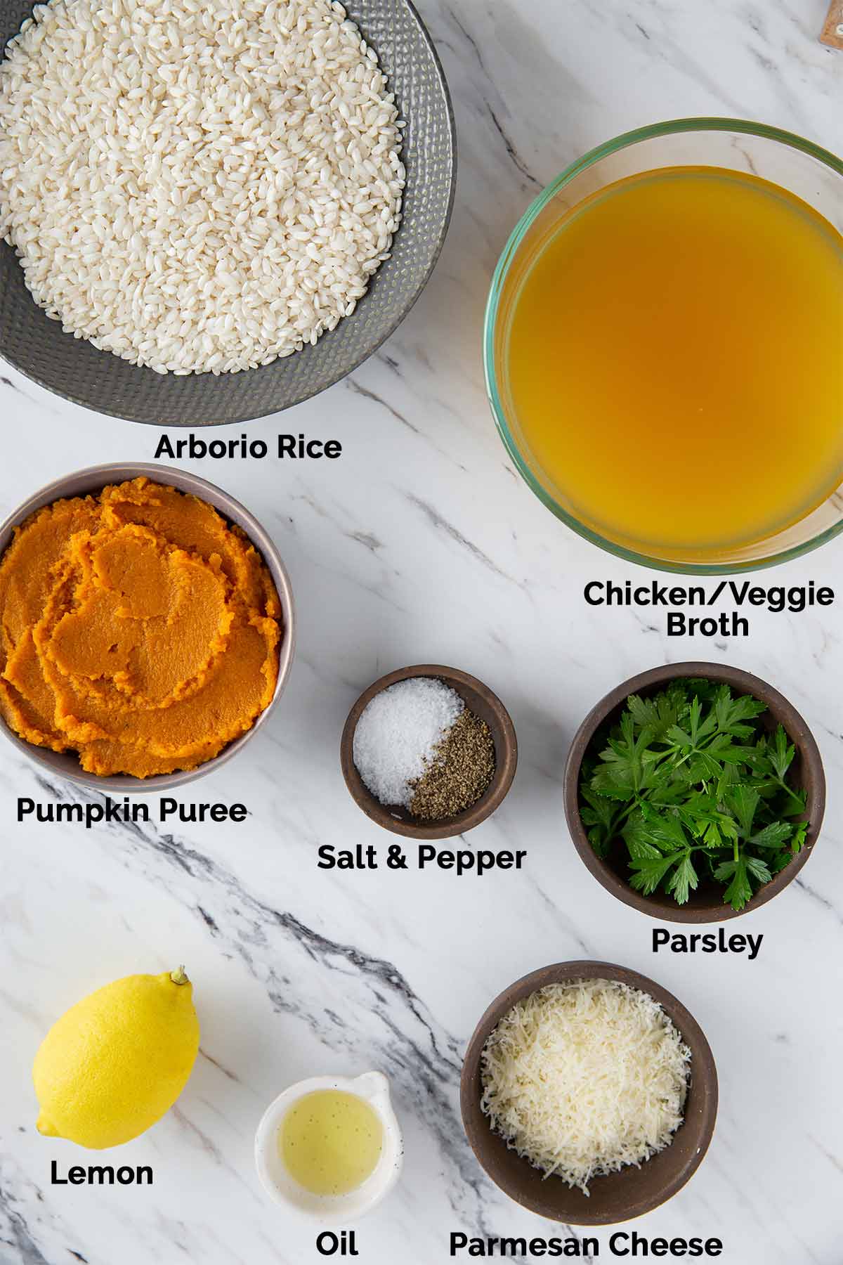 Arborio rice, pumpkin puree, broth, parsley, oil, parmesan cheese, lemon, and seasonings laid on a flat surface for making Instant Pot pumpkin risotto.