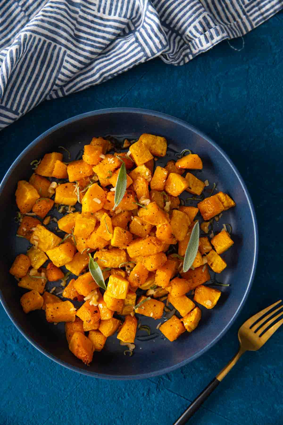 Air fryer roasted butternut squash garnished with sage leaves, parmesan leaves in a serving dish with a napkin on the side.