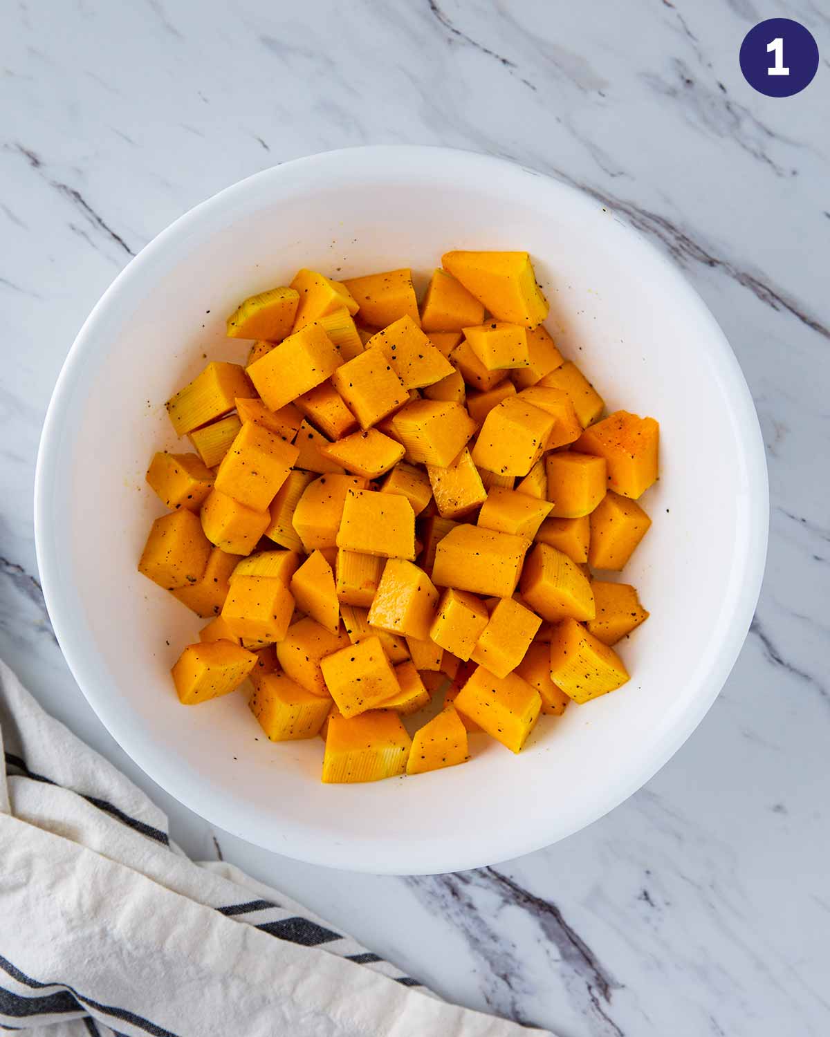 Diced butternut squash in a large mixing bowl after mixing with salt, pepper and oil.