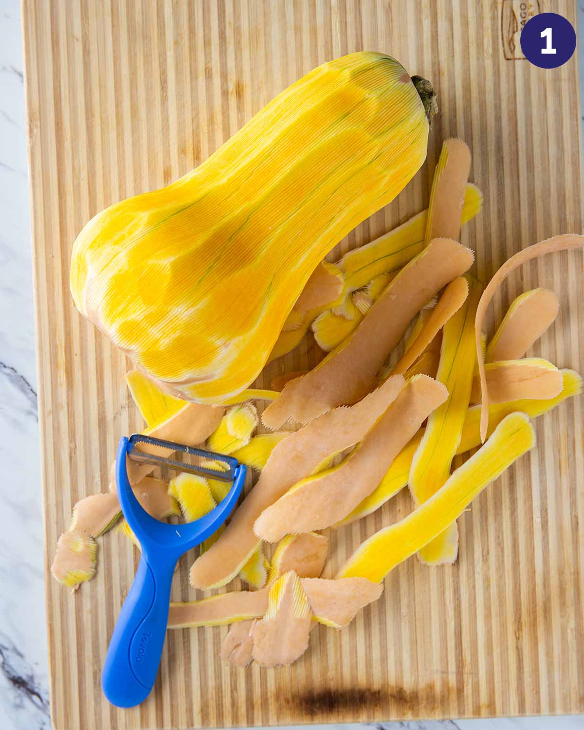 Peeling butternut squash, laid on the cutting board with peeler.