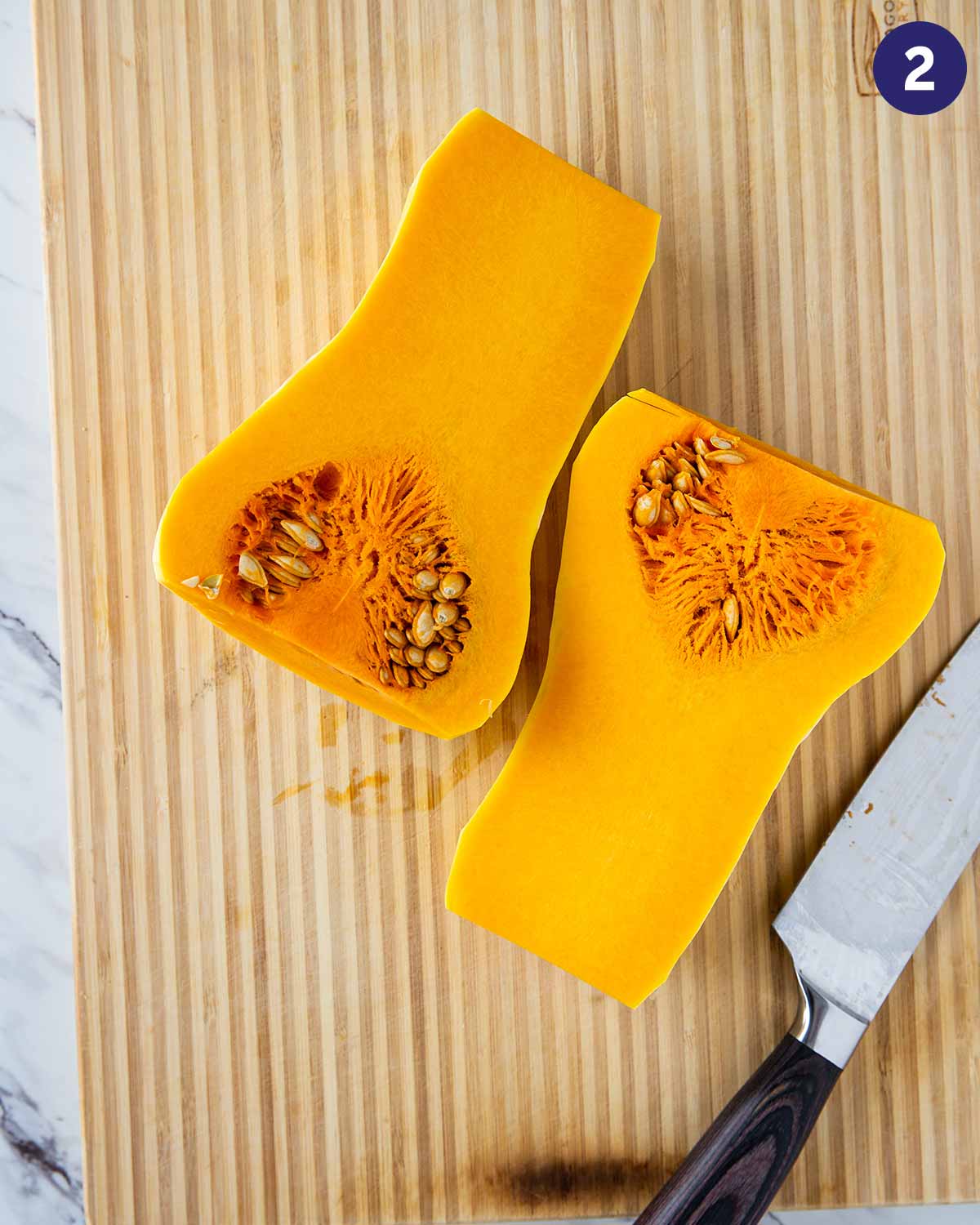 Peeled butternut squash cut into half and placed on a wooden cutting board.