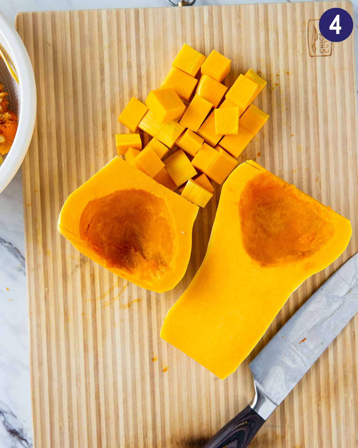 Image shows process of cutting butternut squash into cubes on the wooden cutting board. 