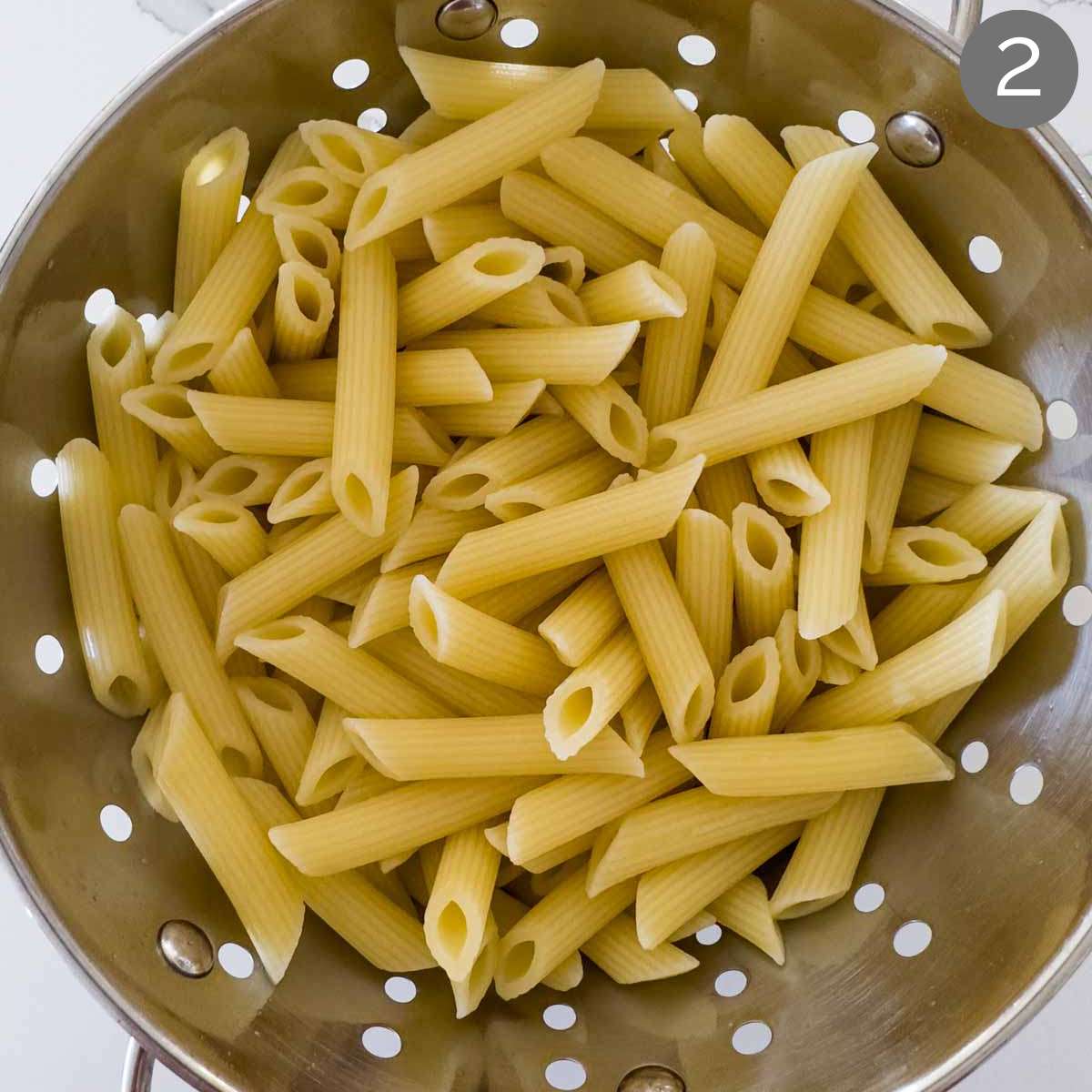 Cooked pasta drained in a stainless steel colander.