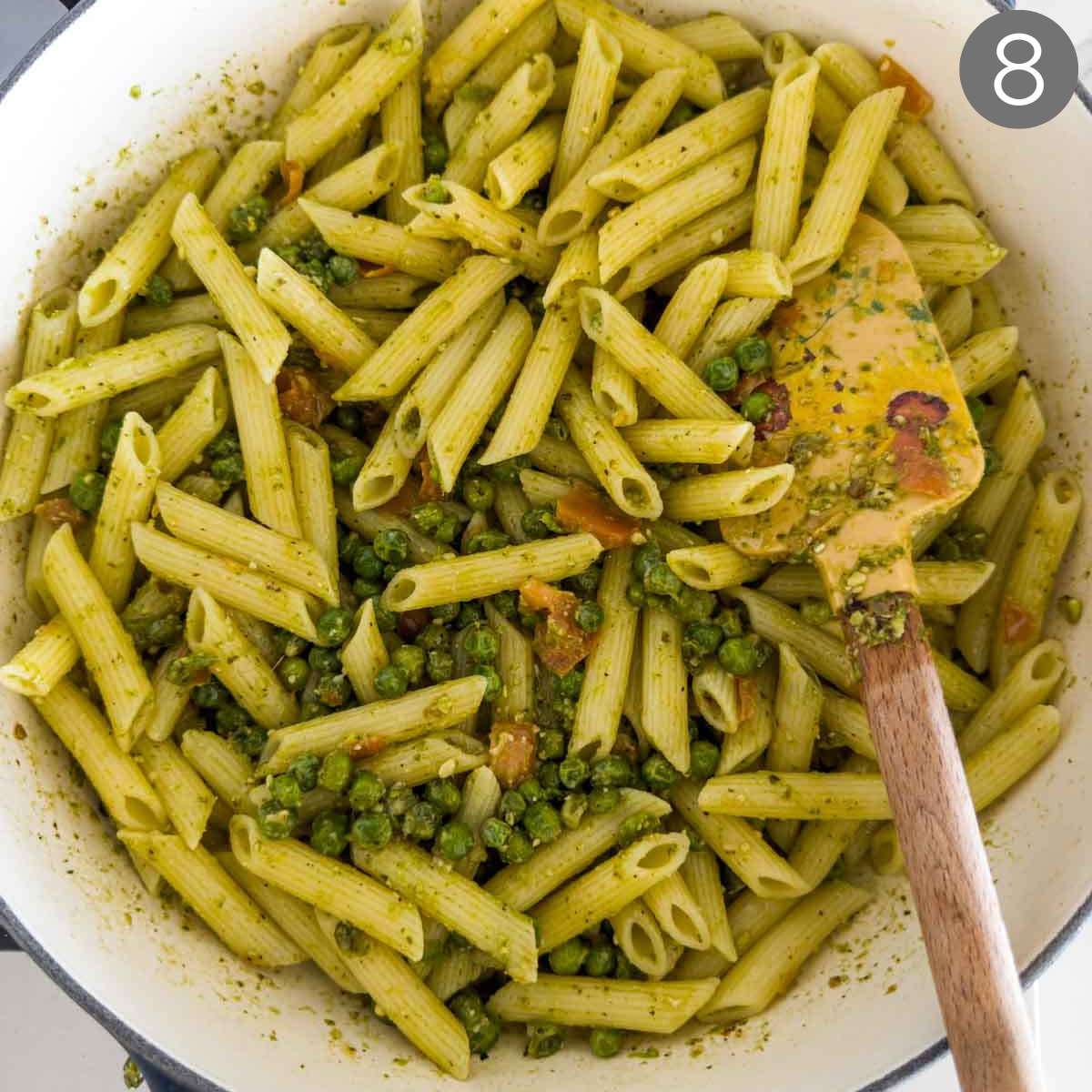 Pasta with peas and pesto in large pan with wooden spatula.