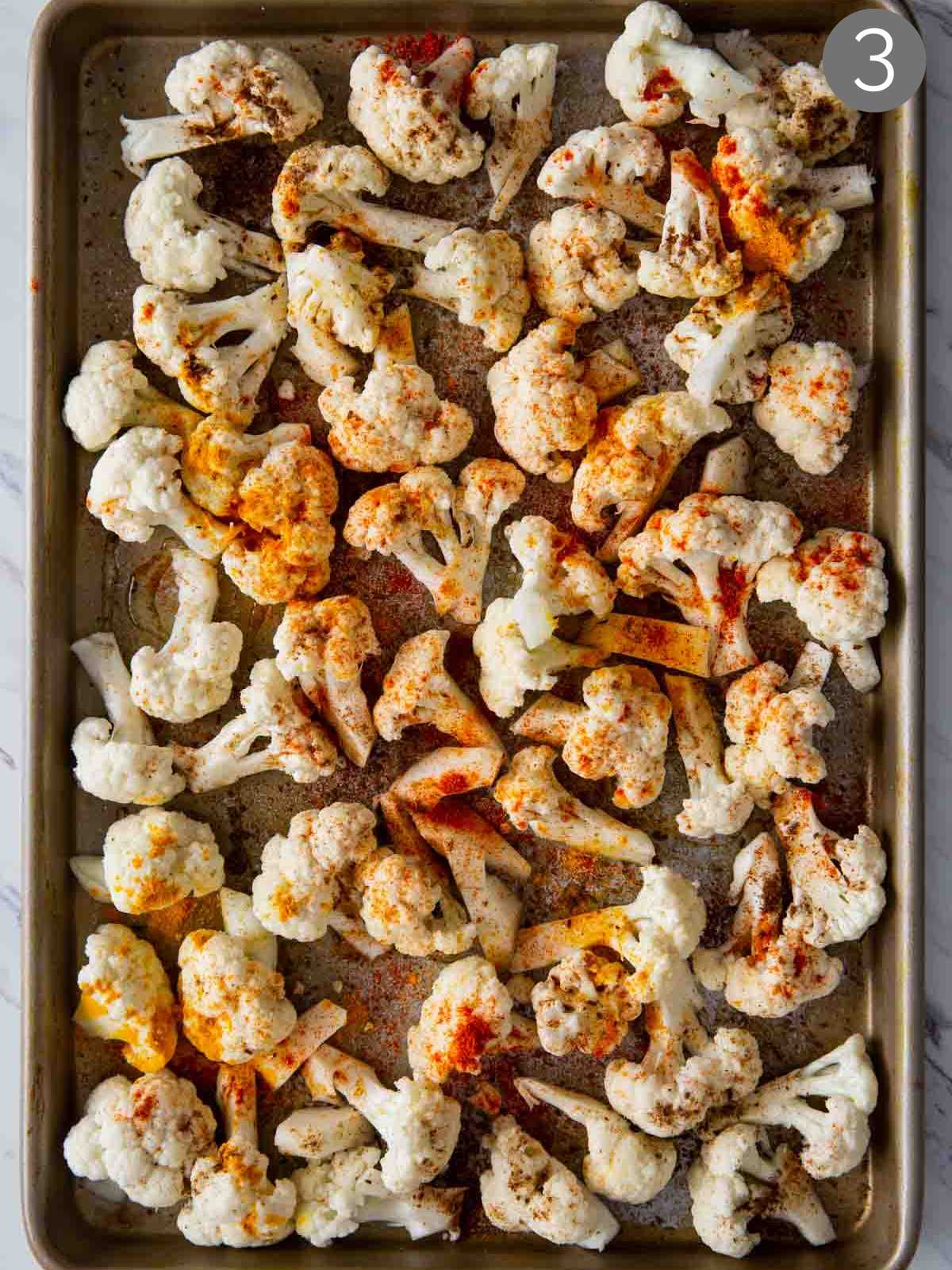 Cauliflower florets sprinkled with turmeric, salt, cumin and paprika on a baking tray. 