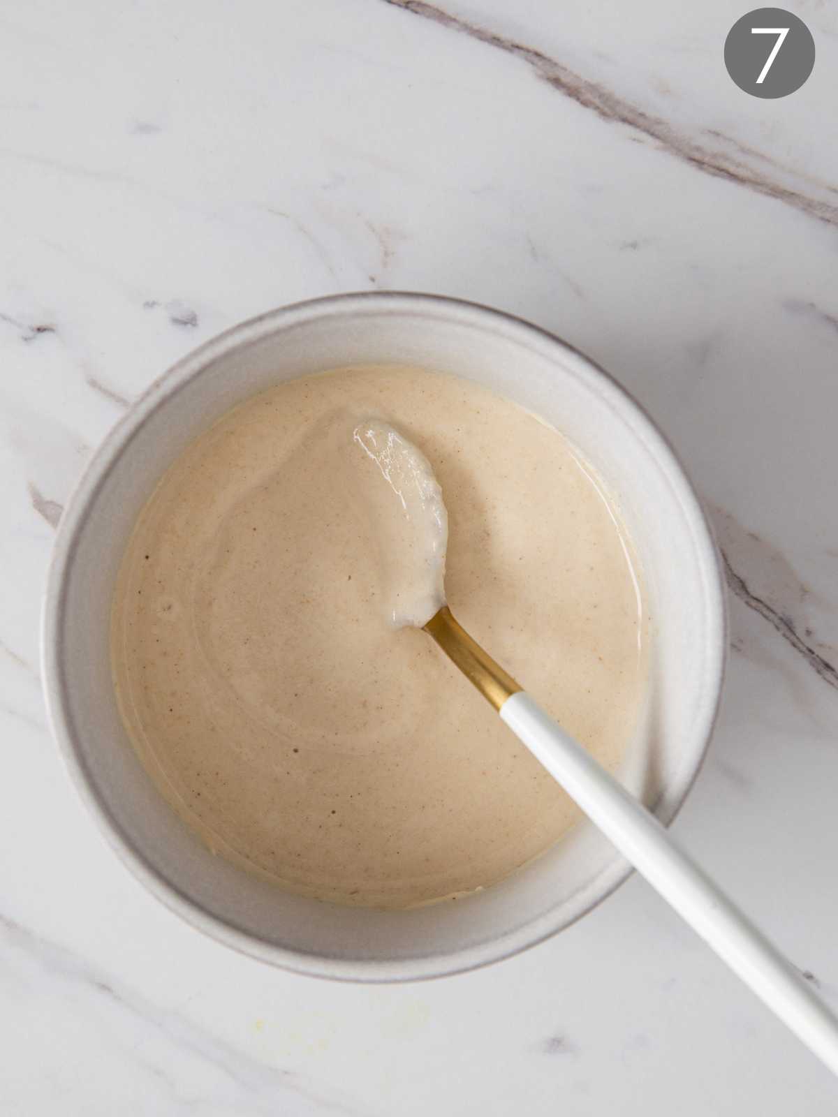 Tahini sauce in serving bowl with a metal serving spoon.