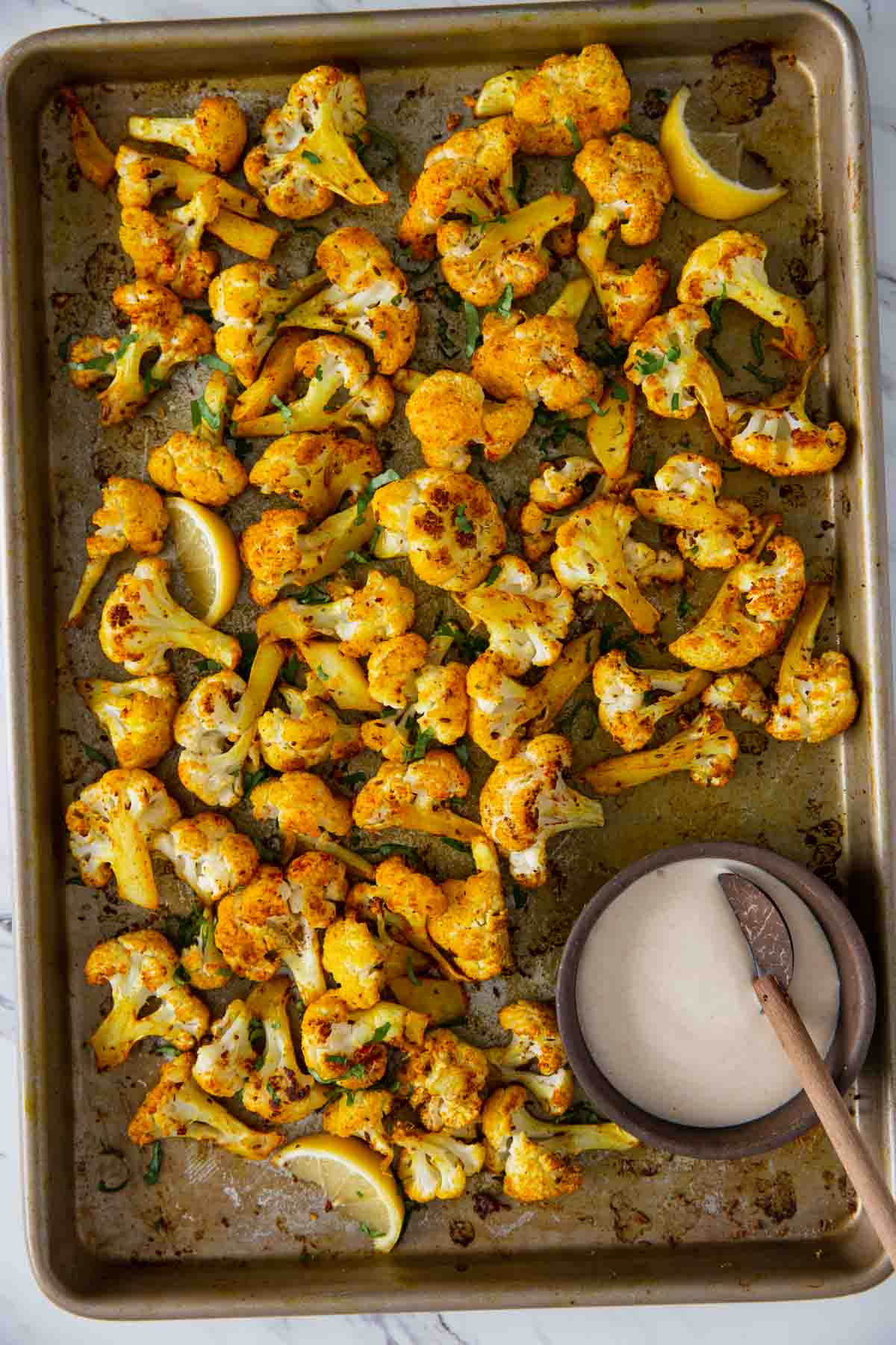 Oven roasted turmeric cauliflower in a baking pan with tahini sauce in a small bowl. 