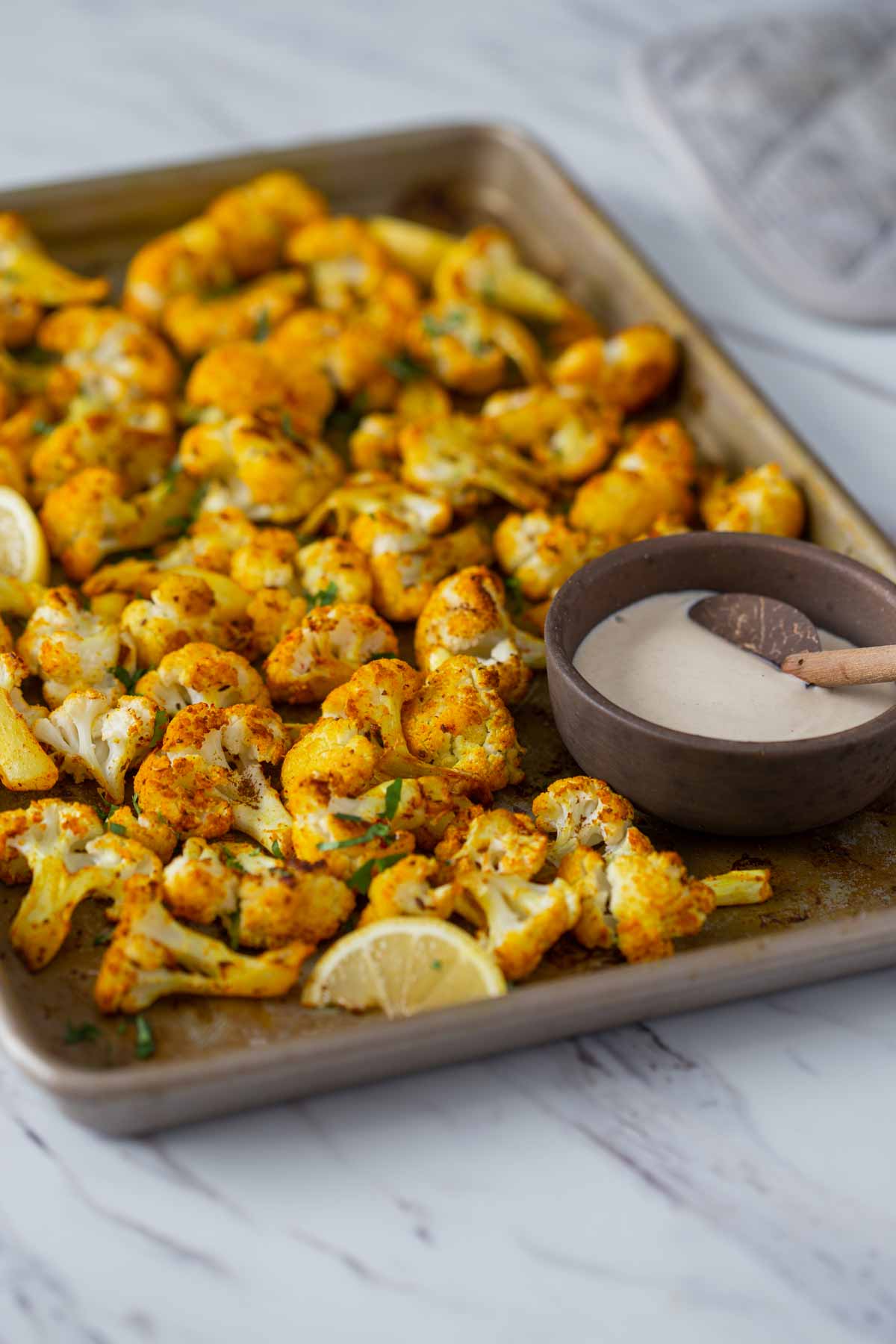 Turmeric roasted cauliflower with tahini sauce on a baking tray.