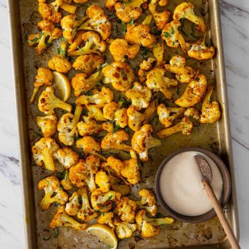 Turmeric roasted cauliflower with tahini sauce on a baking tray.