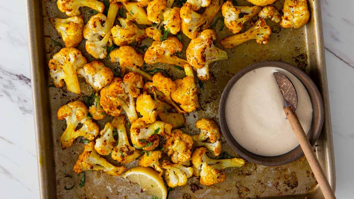 Turmeric roasted cauliflower with tahini sauce on a baking tray.