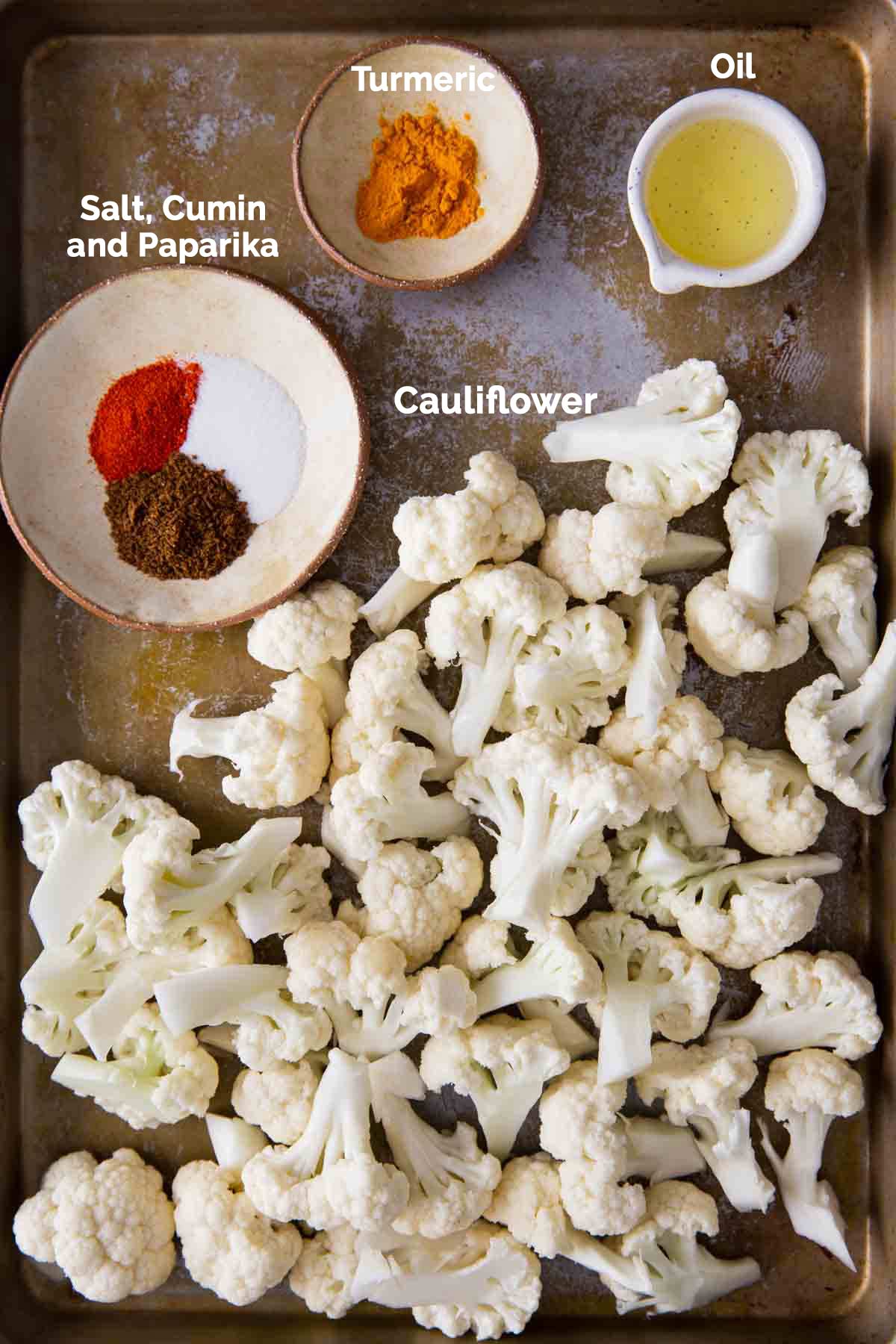 Ingredients to prepare turmeric roasted cauliflower are laid on a flat baking tray.