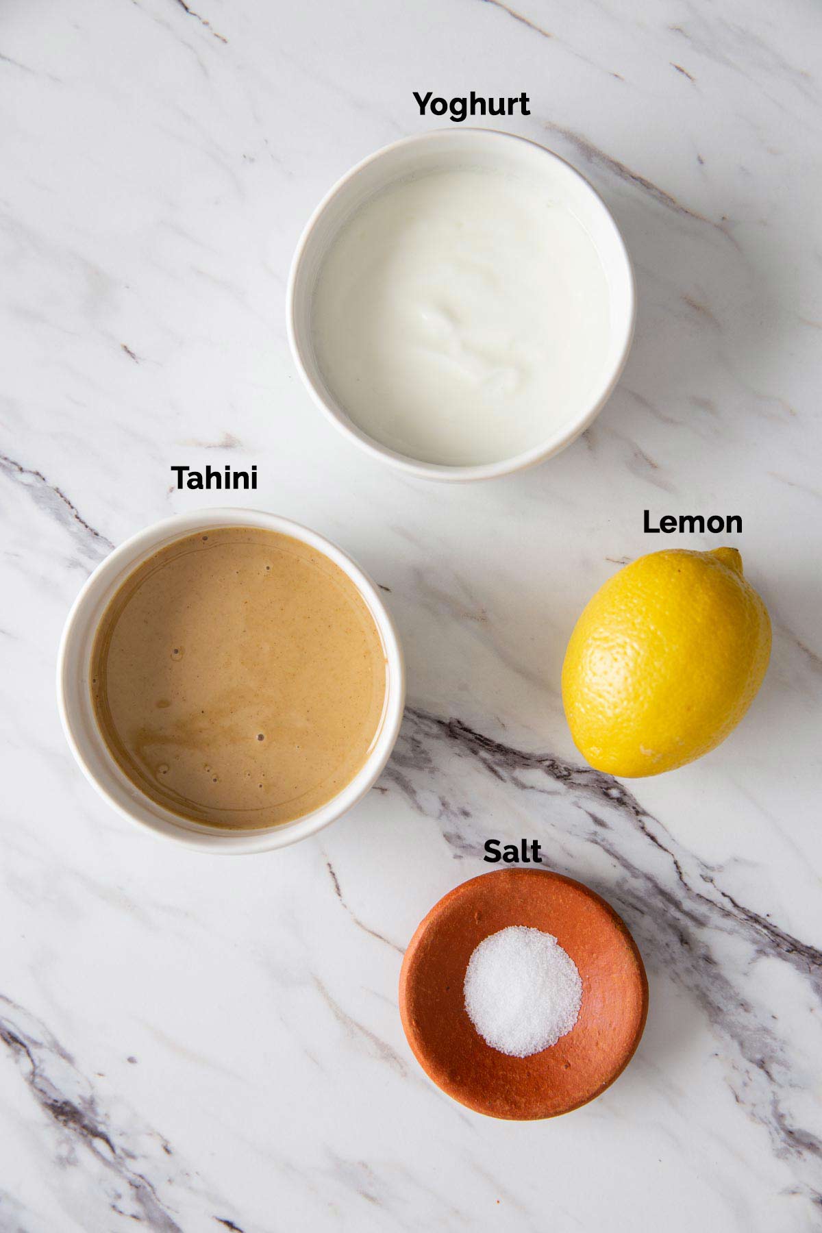 Ingredients to prepare tahini sauce for turmeric roasted cauliflower are laid on a flat surface.