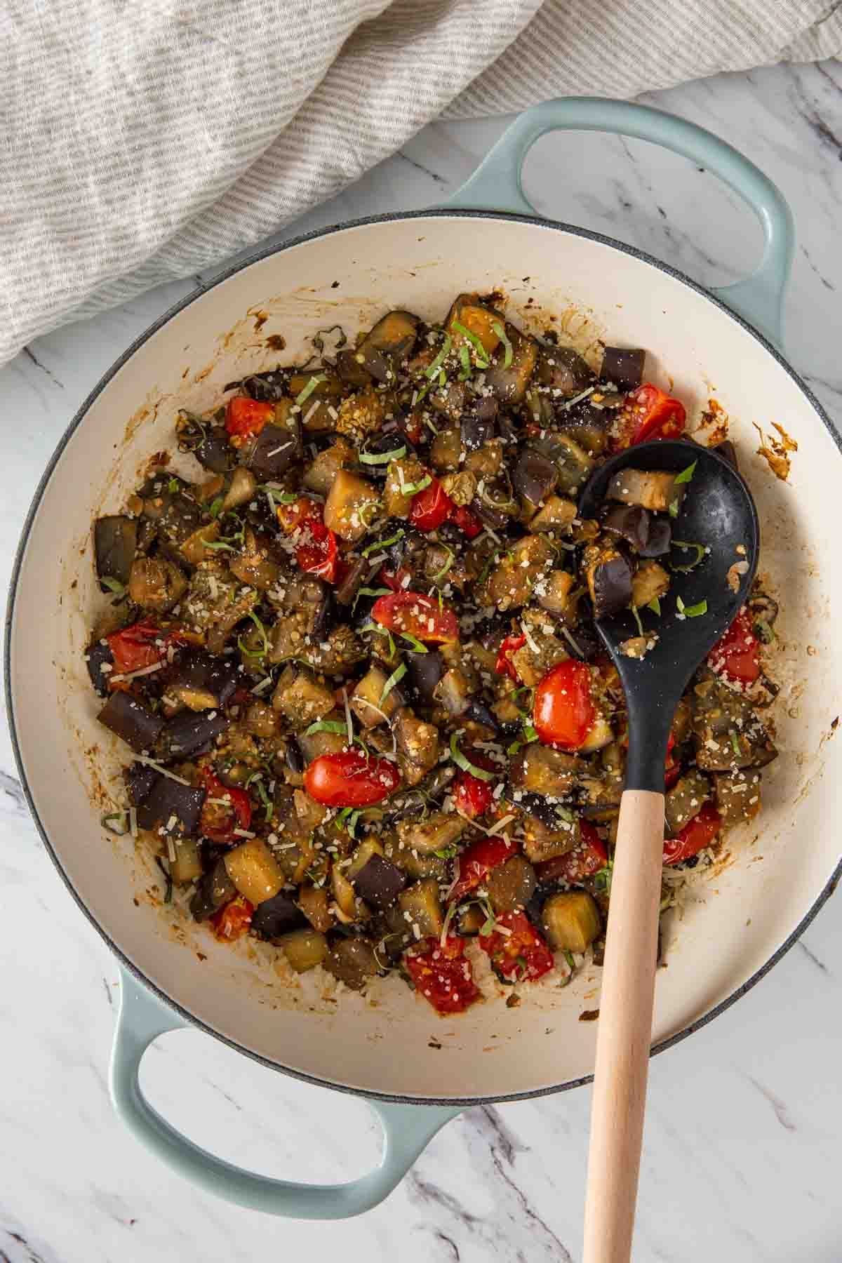 Sauteed eggplant and tomatoes in a large skillet with serving spatula.