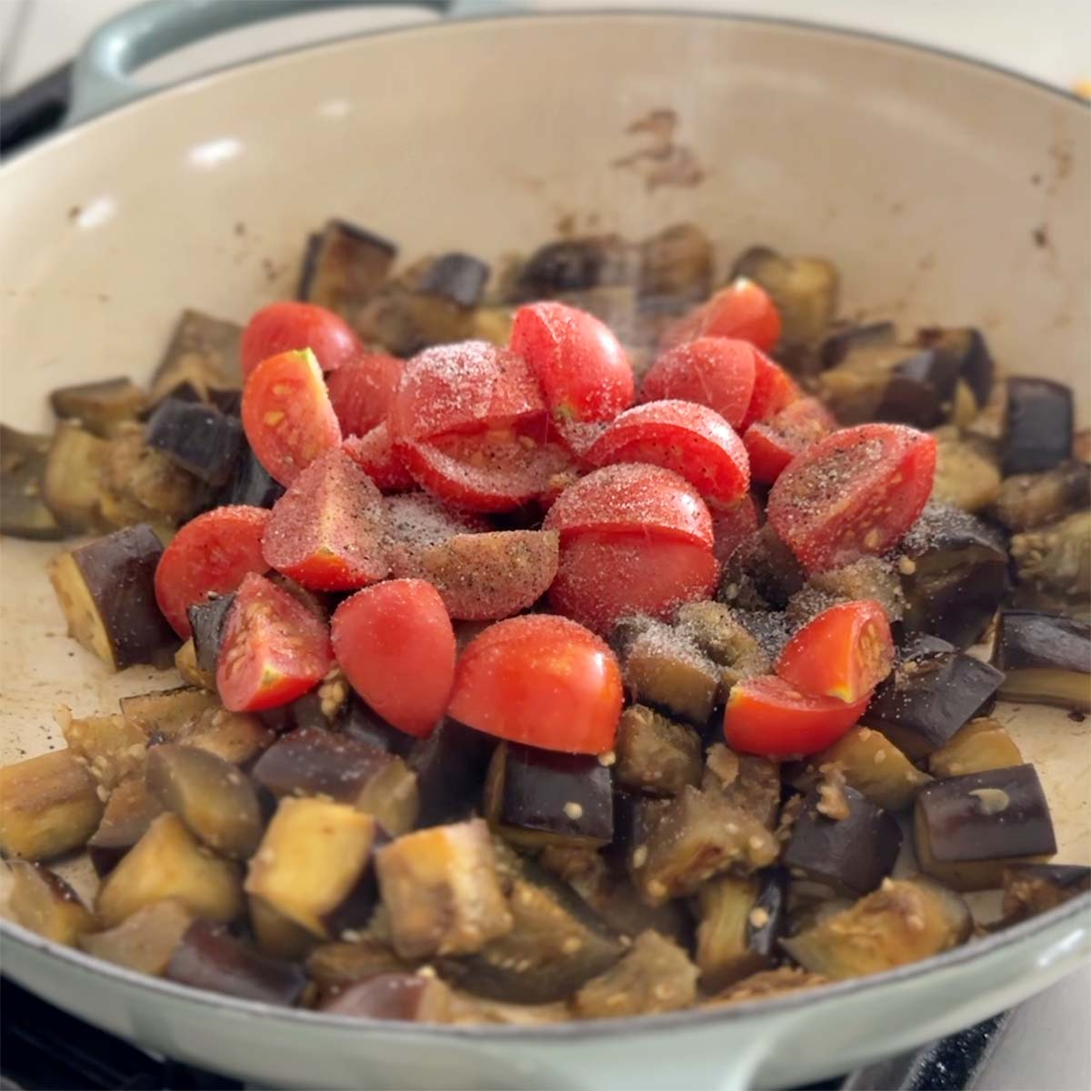 Sauteing eggplant with tomatoes in oil in a large skillet.