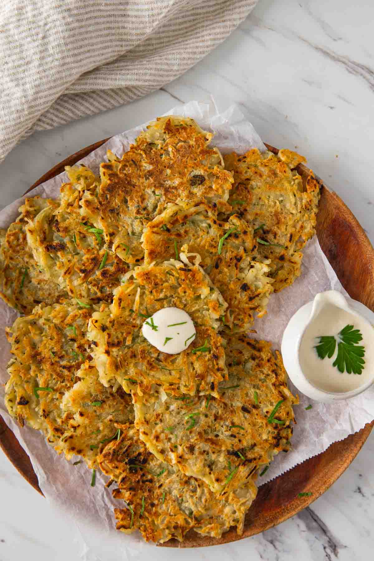 Potato fritters on a wooden plate with dipping sauce on the side.