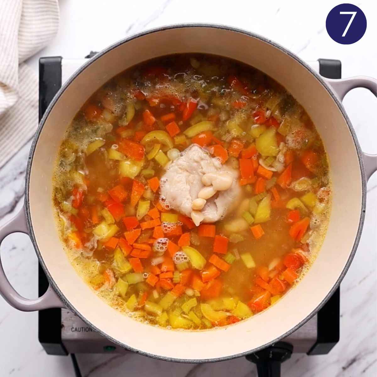 Adding Smashed and whole cannellini beans to the veggie orzo soup in a cast iron pot.