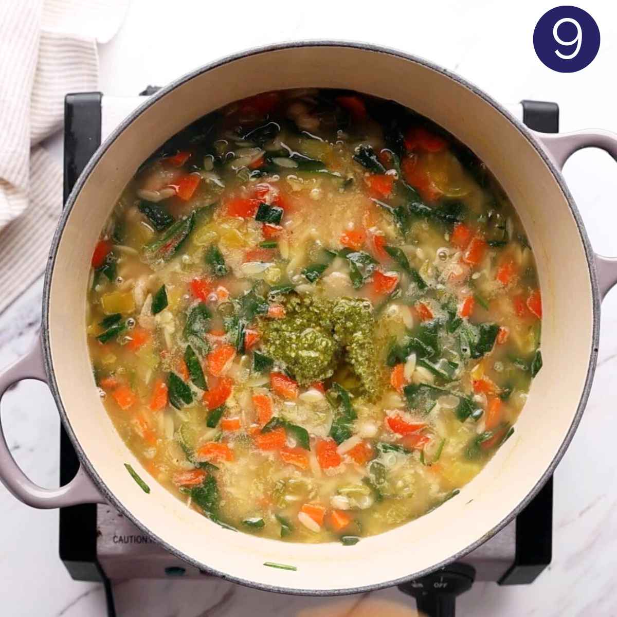 Adding pesto to the veggie orzo soup in a cast iron pot.