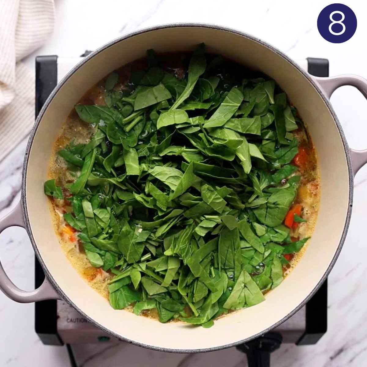 Adding spinach to the veggie orzo soup in a cast iron pot.