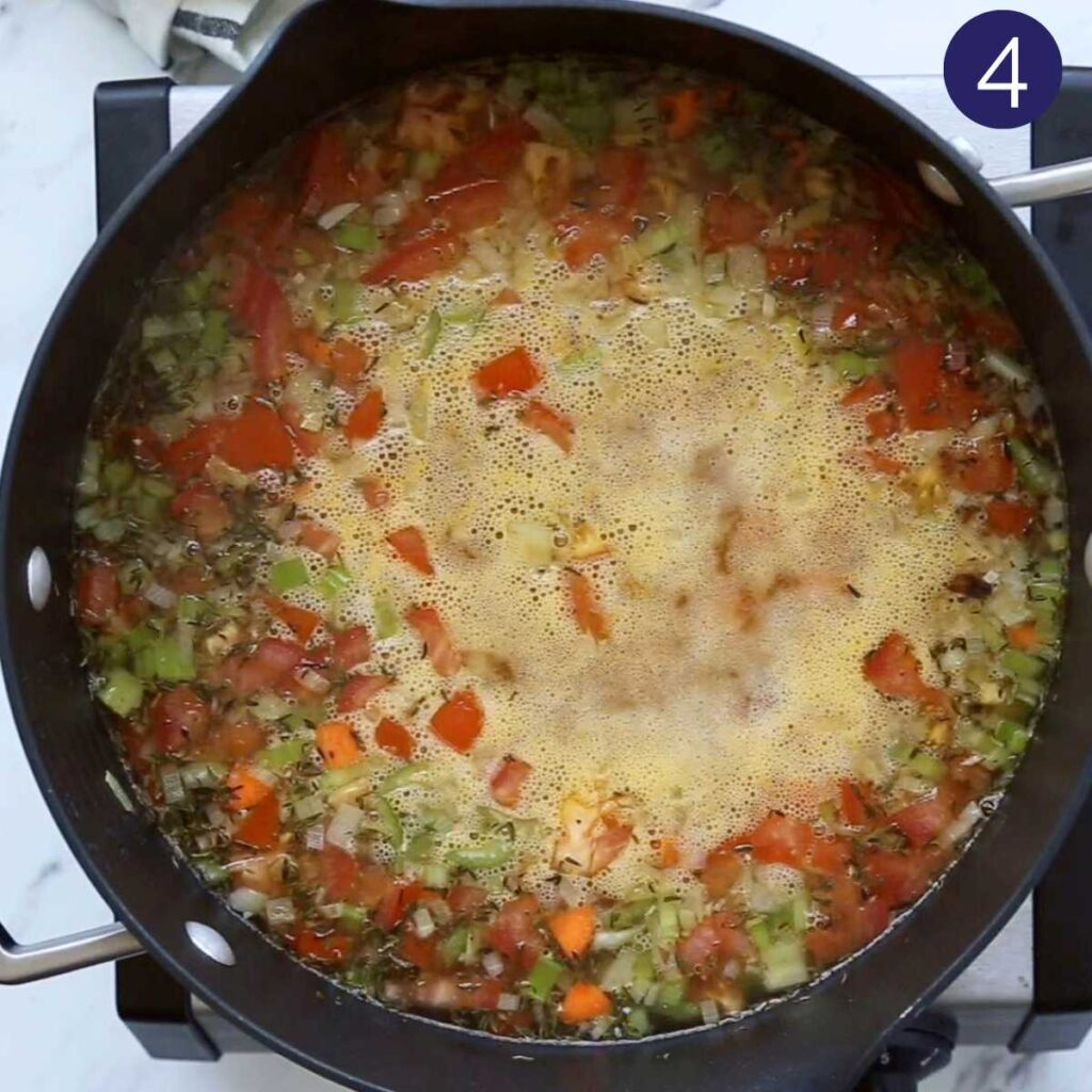 Large pot with diced vegetables, barley and broth to prepare the barley soup.