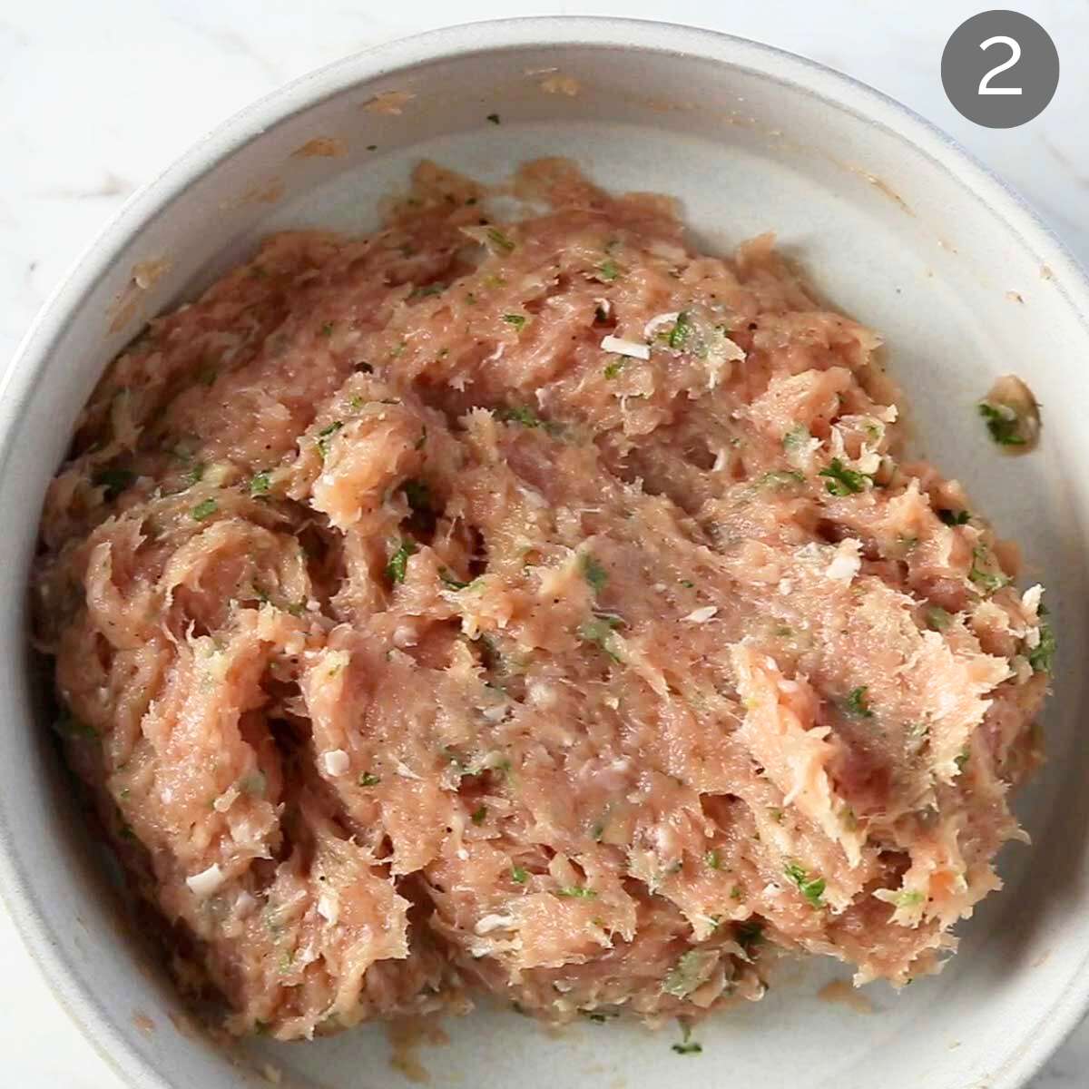 Ground chicken mixed with herbs and seasonings in a mixing bowl.