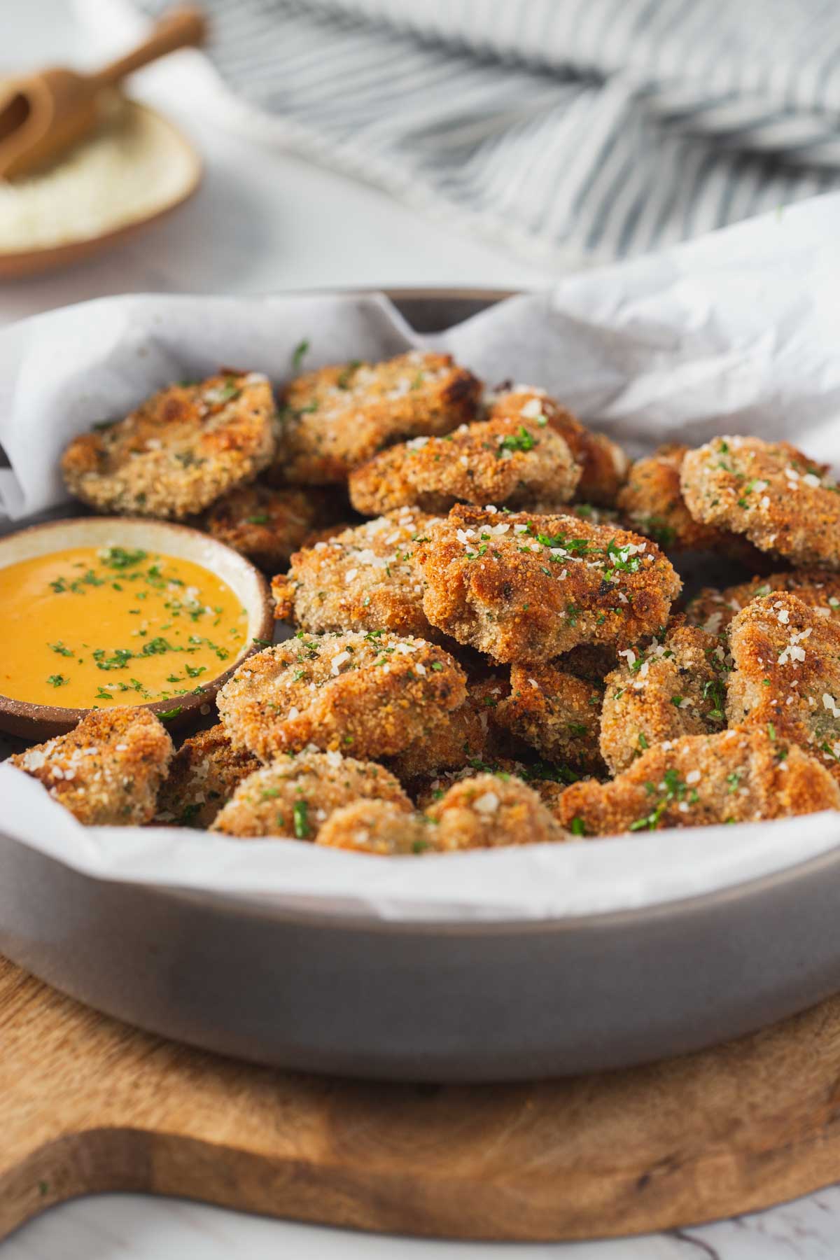 Breaded ground chicken nuggets in a serving shallow bowl with the dipping sauce on the side are ready to serve. 