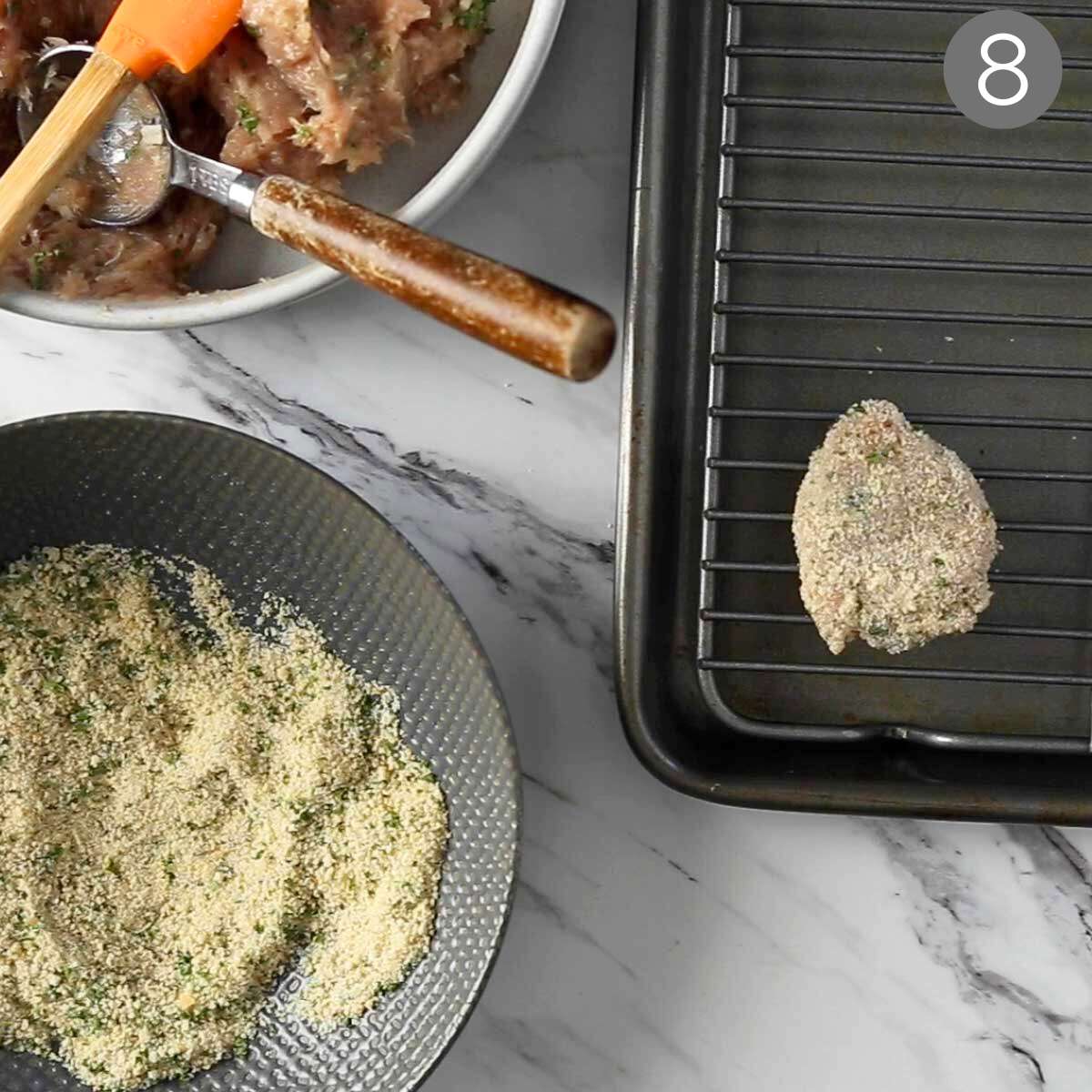 Breaded ground chicken nugget placed on metal rack and bowl of breadcrumbs on the side.