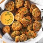 Breaded ground chicken nuggets in a serving shallow bowl with the dipping sauce on the side are ready to serve. The bowl is placed over a round wooden board.