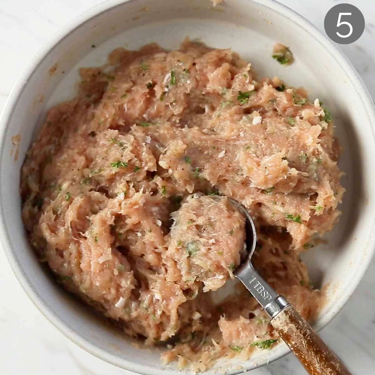 Ground chicken in a mixing bowl with a measuring tablespoon.