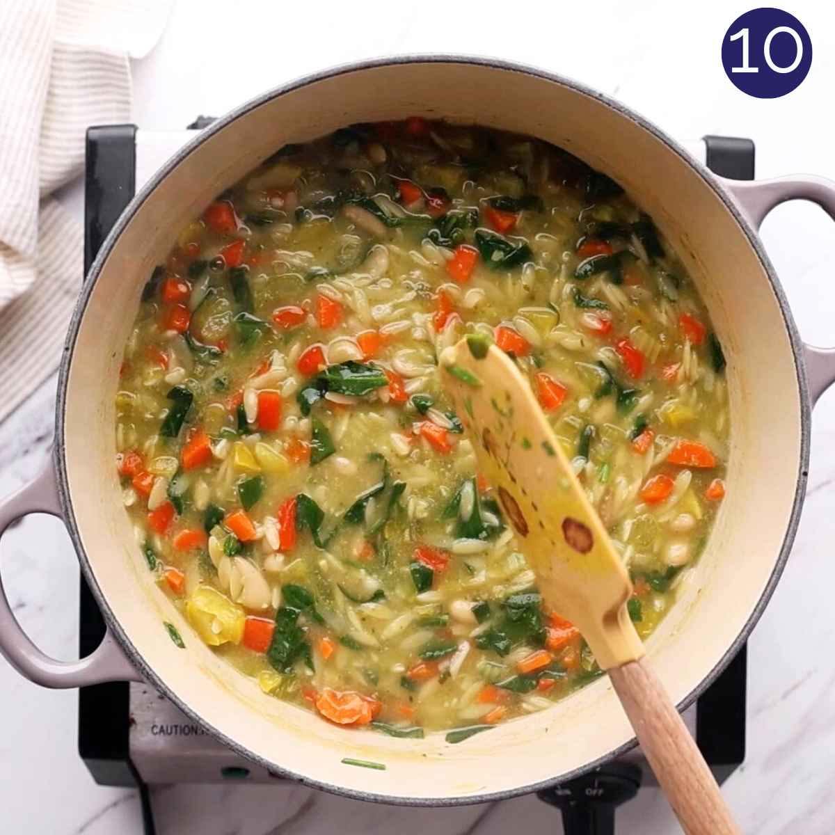 Mixing pesto in the veggie orzo soup in a cast iron pot.