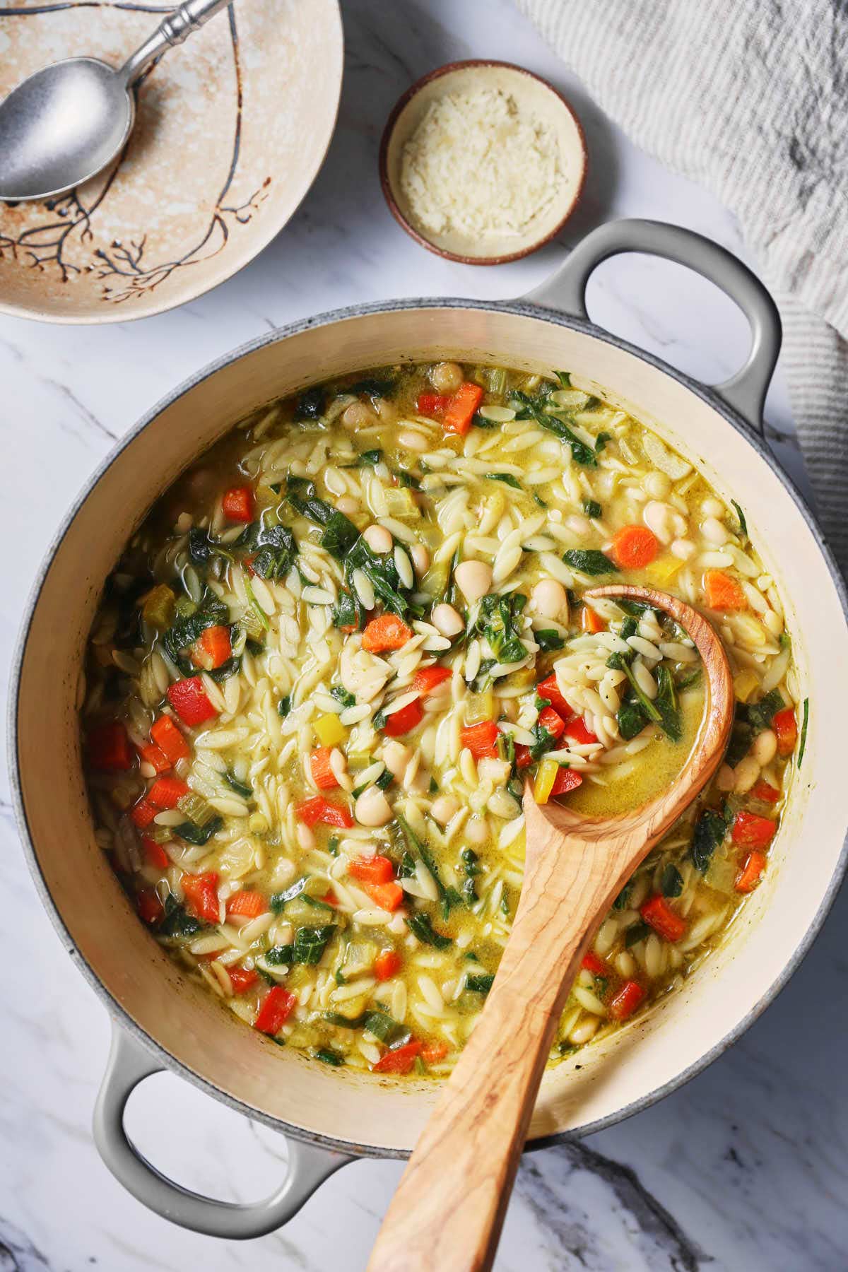 Pesto and vegetable orzo soup in large pot with a wooden laddle. 