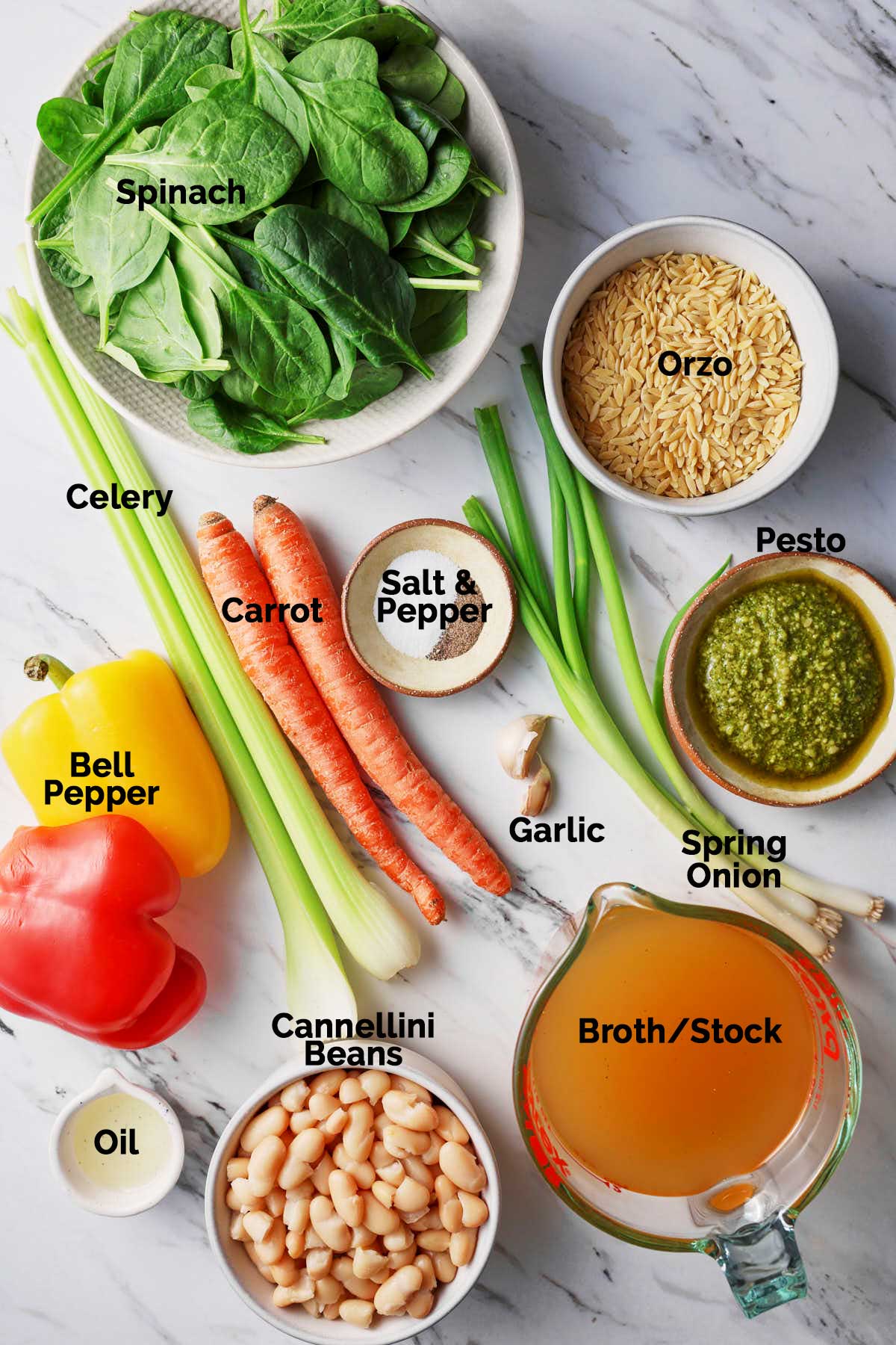 Ingredients to prepare vegetable orzo soup with pesto are laid on a flat surface.