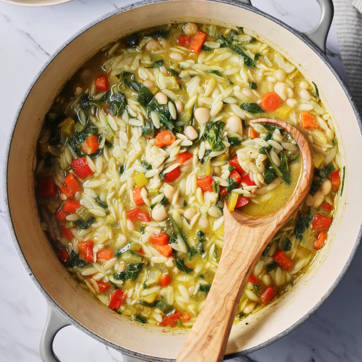 Pesto and vegetable orzo soup in large pot with a wooden laddle.